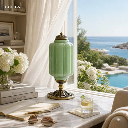 Green lamp on a table with a scenic view of a pool and ocean.