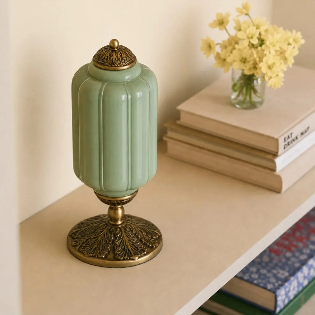 Decorative green and gold lamp on a shelf with books and flowers