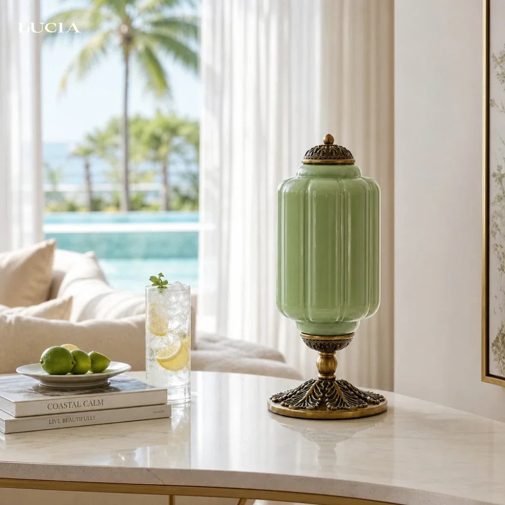 Decorative green lamp with gold base on a table by a window with a view of palm trees and a pool.